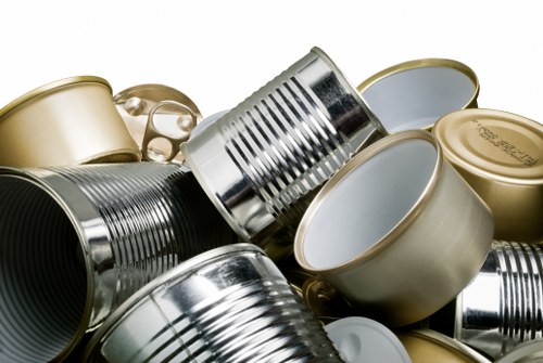 A collection of empty, discarded cans made of tin and aluminium, piled together and resting on a flat surface. The cans vary in size and shape, with some appearing crushed or flattened, while others are intact. Many of the cans have neutral or metallic finishes, with some showing reflective surfaces and others displaying duller, matte textures. The background includes a neutral grey or white setting, focusing attention on the cans. The scene depicts typical waste items collected for rubbish removal, which a service like Garden Clearance Harrow might handle during garden or property clearance in the Harrow area. The image emphasizes the need for proper disposal or recycling of metallic waste materials, aligning with professional rubbish removal practices.